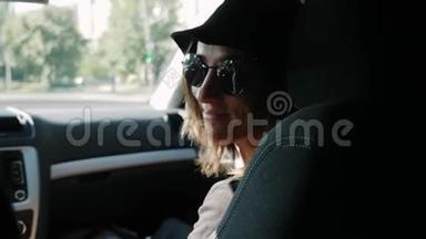 英俊的白种人女人戴着黑色帽子和太阳镜坐在出租车里。 坐在<strong>副驾驶</strong>座上的快乐微笑的女人